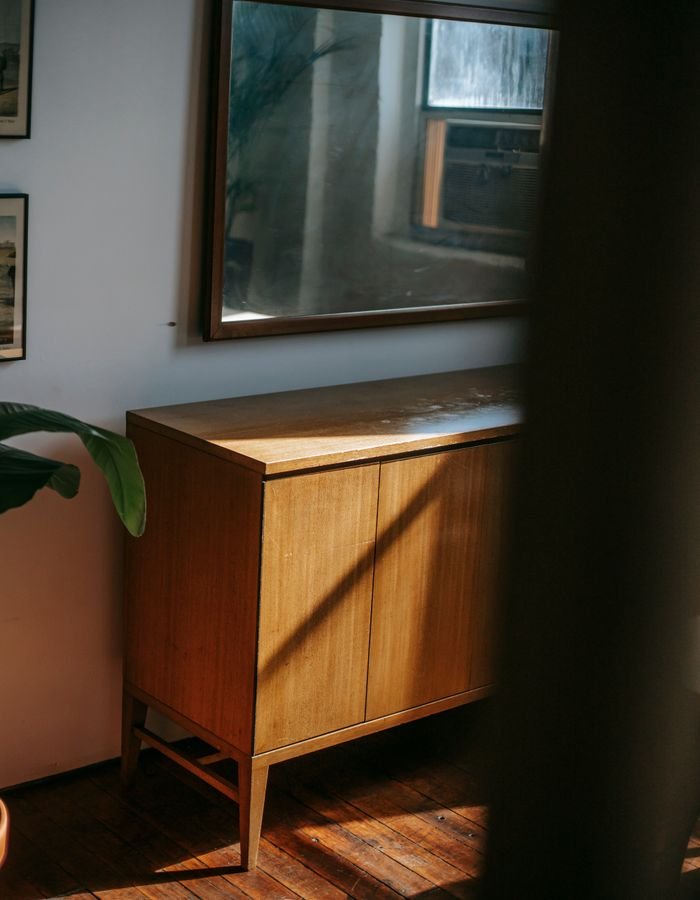 A framed mirror hanging above a teak sideboard in warm afternoon light