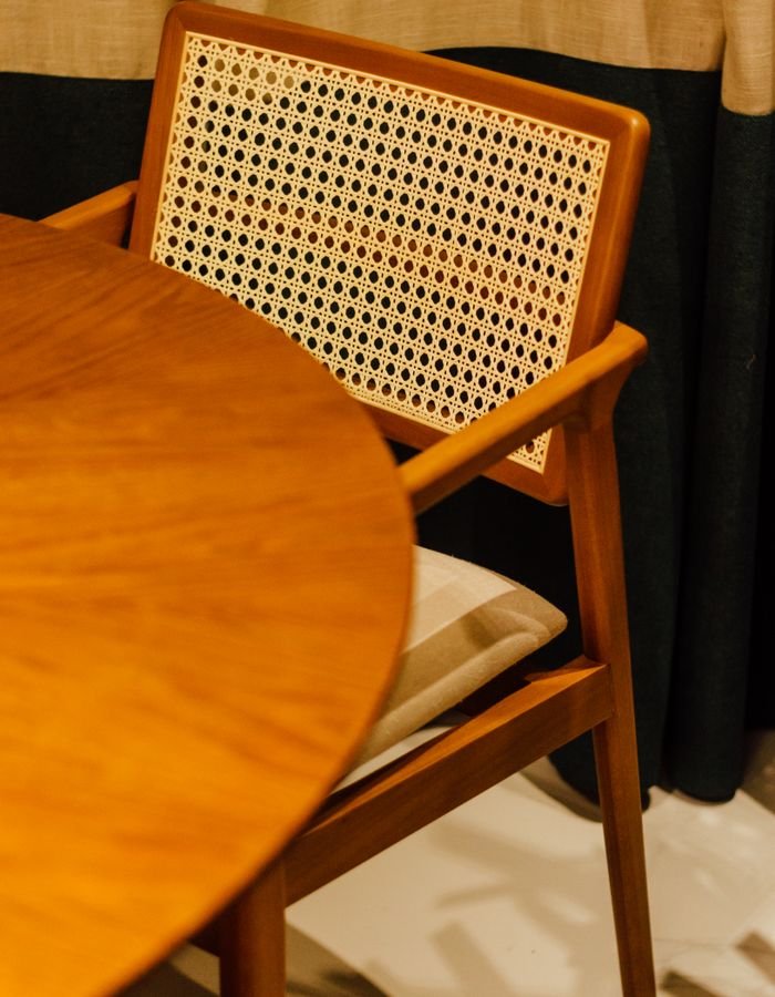 A round wooden table beside a caned mid-century dining chair