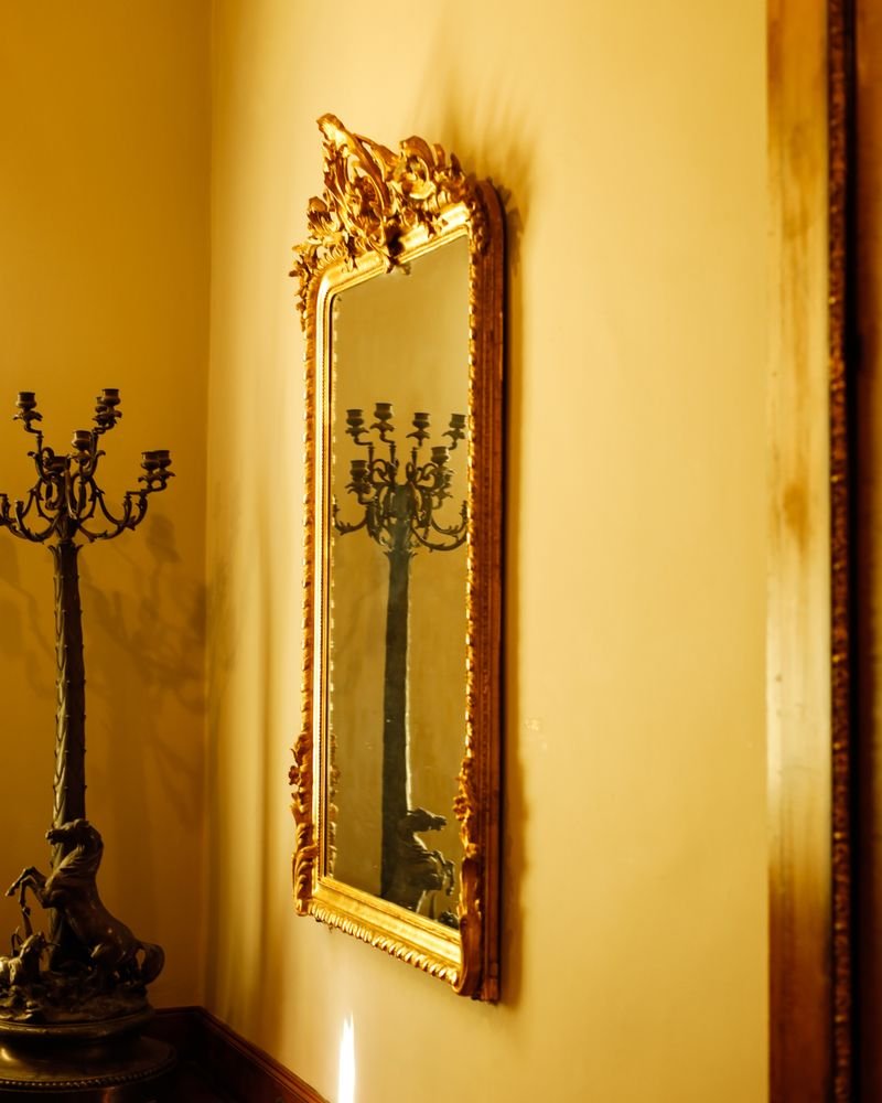 A giltwood mirror with an ornate carved crest on a warm painted wall