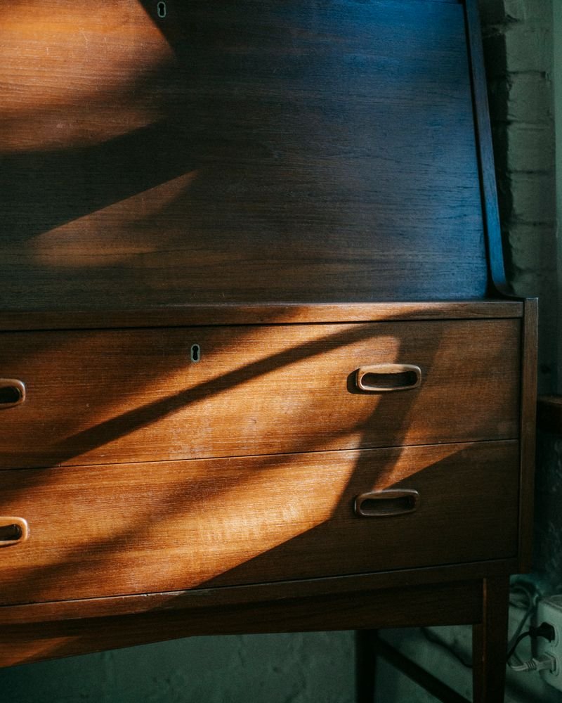 A teak fall-front bureau lit by raking afternoon sunlight