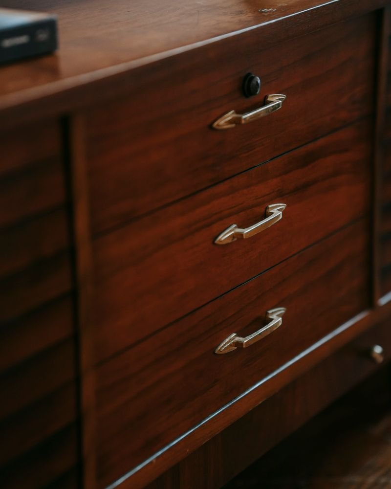Close detail of a walnut credenza drawer front with sculpted brass pulls