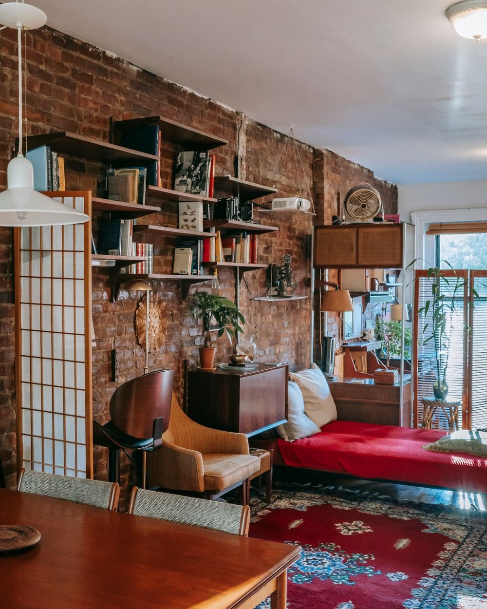 A warm loft interior with exposed brick, teak shelving and a curated mix of vintage furniture